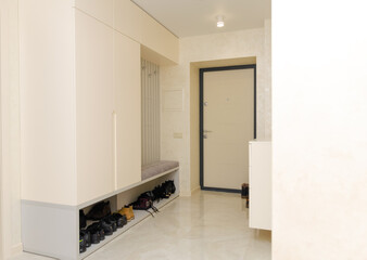 Beautiful modern entrance hall in light, white colors with a wardrobe, hooks for clothes, a chest of drawers for shoes