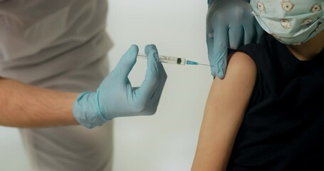 Close up shot of little boy kid in protective medical mask getting vaccinated. Unrecognizable male doctor injecting vaccine into child's shoulder.