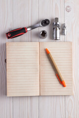 Ratchet wrench with replaceable nozzles and notebook with pen on white wooden background.