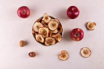 A bowl of dried apple pieces, a few ripe red apples and walnuts on a light surface. The concept of useful products. Selective focus.