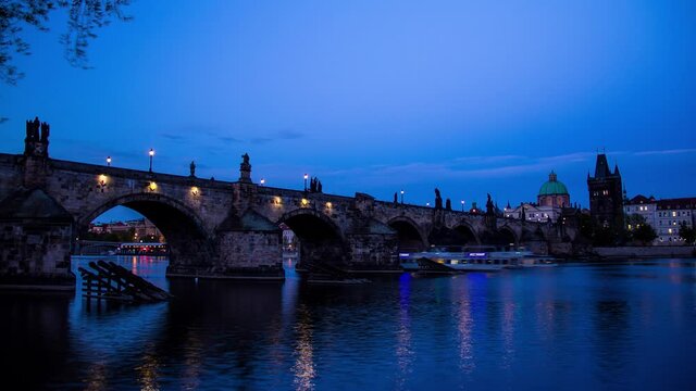 Day to night sunset timelapse as the Charles Bridge in Prague, Czech Republic lights up during the evening with a view of the Old Town bridge Tower