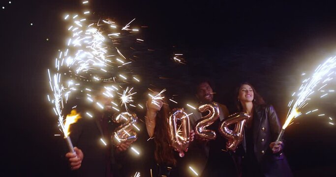 Group of friends celebrating new years holding 2024 balloons and sparklers