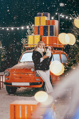 New Year's and Christmas. Woman in front of a red retro car. Snowfall, lights. Christmas mood.