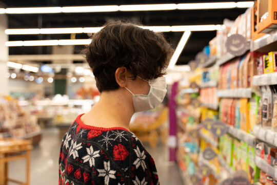 shopping woman wearing medical mask short hair at the grocery store for christmas or new year dinner table. ugly christmas sweater. coronavirus times pandemic. blurry photo. diversity. social distance