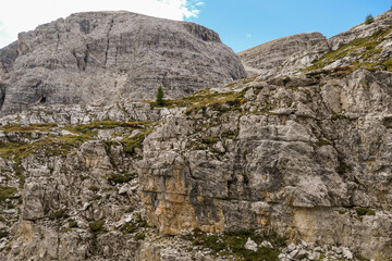 A close up view on a massive, high and desolated mountain wall in Italian Dolomites. The wall has sandy color with some darker shades. Dangerous climbing route. Few green plants on the steep slopes.