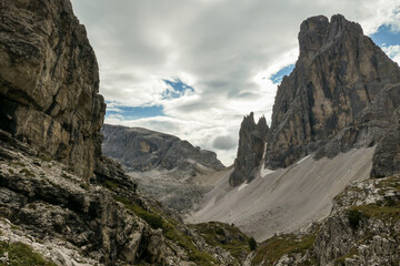 A panoramic view on Italian Dolomites. There are many high and sharp peak in front, with many landslides. Dangerous climbing. Barely any plants growing in the area. Raw and unspoiled landscape.