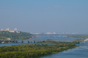 Aerial view of the river with island coated by green trees, in the foreground and several bridges over the river with city districts in the background. 