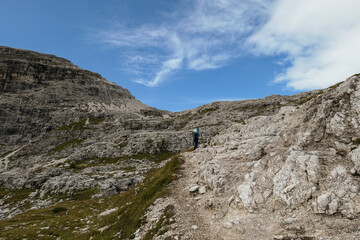 A woman hiking in a high and desolated mountains in Italian Dolomites. The lower parts of the mountains are overgrown with moss and grass. Raw and unspoiled landscape. Clear and sunny day. Solitude