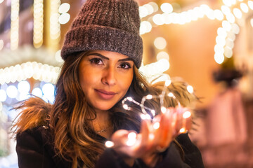 Christmas portrait with christmas lights in a beautiful building in the city, young caucasian woman at night with some beautiful lights in her hand. With a winter hat
