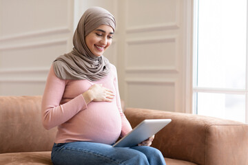 Joyful Pregnant Muslim Lady Using Digital Tablet Sitting At Home