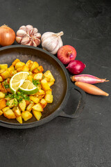front view tasty fried potatoes inside pan with lemon and garlics around on dark background color meal food calorie