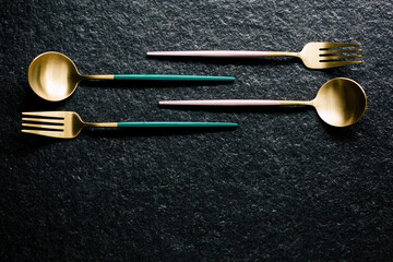 set of pink, green and gold forks and spoons on a black background. Flat and top view. Modern food....