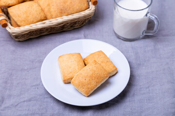Cookies on a white plate. In the background, a basket of cookies and a cup of milk. Close-up.