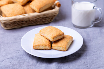 Fototapeta na wymiar Cookies on a white plate. In the background, a basket of cookies and a cup of milk. Close-up.