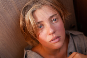 soft portrait of beautiful young blonde woman without make-up in gray linen shirt in wooden interior with sunlight