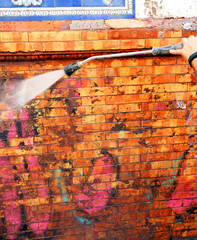 Worker cleaning graffiti in a dirty facade with high pressure water