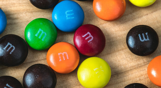 Chocolates M&Ms em close up sobre objeto de madeira.