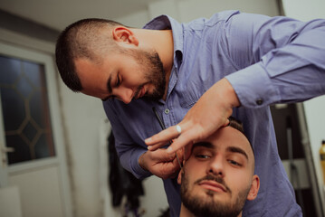 barber shaving bearded male with a sharp razor in a saloon.
