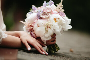Wedding. The girl in a white dress and a guy in a suit sitting on a wooden chair, and are holding a beautiful bouquet of white, blue, pink flowers and greenery, decorated with silk ribbon