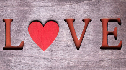 The word love with red heart on wooden background.  