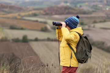 Little boy exploring the hill with binoculars in autumn day.