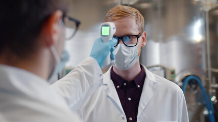 Close up of manager measuring body temperature of workers with infrared thermometer at factory