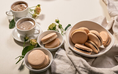 Delicious french macaroons and Frothy coffee in white cups. Dessert still life on a beige background. Close-up