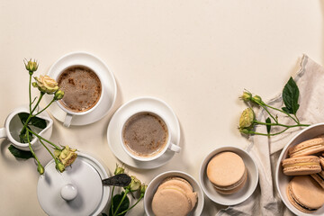 Coffee in white cups, delicious french macaroons. Dessert still life on a beige background. Vertical shot. Copy space