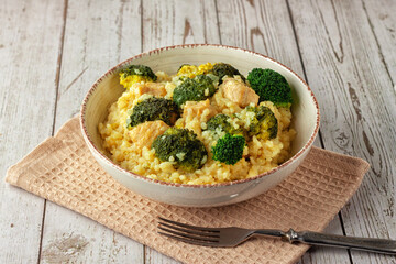 Creamy risotto with chicken and broccoli on wooden background