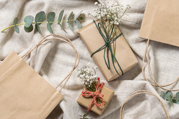 Eco friendly zero waste holiday composition with gift boxes in craft recycling paper decorated with dry flowers, paper bags, fresh eucalyptus twigs on natural linen fabric background top view.