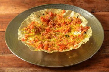 Masala Papad is a delicious Indian snack made using roasted or fried papad topped with a tangy and spicy onion tomato mix, served over a rustic wooden background, selective focus