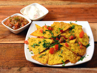 Nachos Cheese and salsa - A classic Mexican appetizer made from corn tortilla chips with cheese and salsa served over a rustic wooden background, selective focus