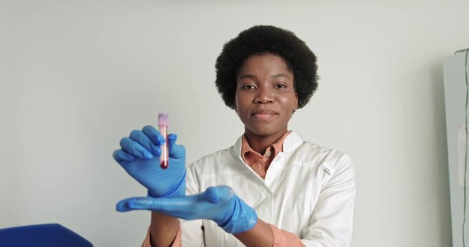 Female african scientist doctor doing blood test in laboratory. Covid 19 test. Doctor virologist raises hand, shows blood test tube. Vaccine, disease cure