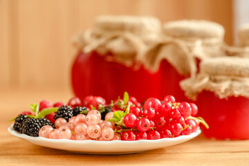 Assorted fresh summer berries and jam in jars. Raspberries, gooseberries, blackberries, currants, wild strawberries, strawberries.
