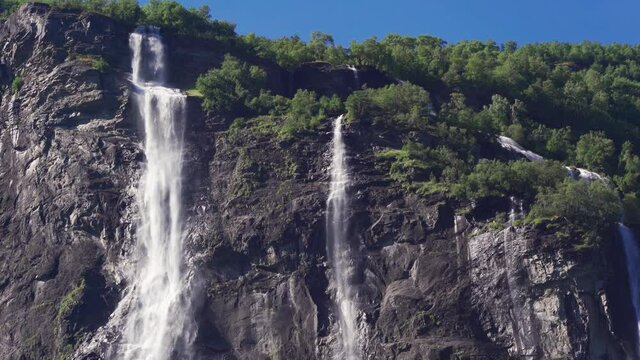 The Sven sisters waterfall - an iconic feature of the Geiranger fjord, Norway. Seven steams falling from 250-meter cliffs joining with the fjord. Deserted farm Knivsfl&aring; sitting on the top of the falls