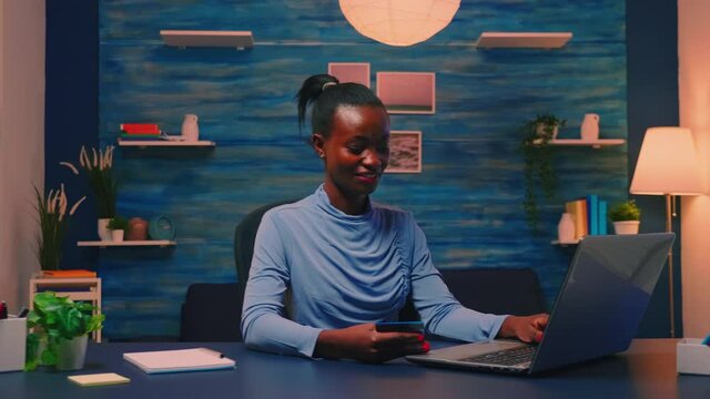 Black business woman making transaction from home using credit card sitting in living room late. Freelancer shopping online from home with electronic paymant on digital notebook conected to internet