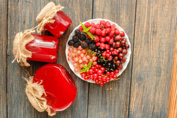 Assorted fresh summer berries and jam in jars. Raspberries, gooseberries, blackberries, currants, wild strawberries, strawberries.