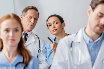 Fototapeta premium Concentrated multicultural colleagues looking away during meeting on blurred foreground in hospital