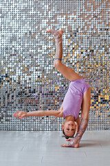 a young beautiful gymnast in sports clothes performs gymnastic poses. Training, an element of gymnastics, acrobatics on a shiny background. sports motivation, stretching, banner for advertising