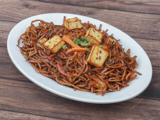 Paneer Noodles a popular indo-chinese dish served over a rustic wooden background, selective focus