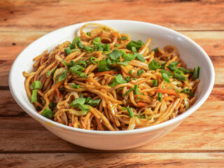 Veg Hakka Noodles a popular oriental dish made with noodles and vegetables, served over a rustic wooden background, selective focus