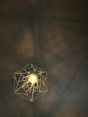 Geometrical golden yellow chandelier on gray ceiling. Illuminating light with shadow lines. Text space