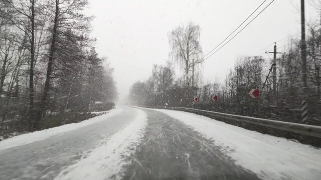 View through the windshield on the highway in winter along which the car is driving in heavy snow and wind in Russia.