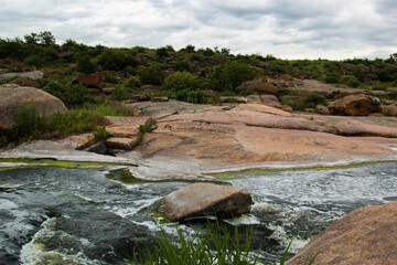 Waterfall flows among high rocks, red stones and cliffs, green bushes and trees