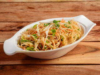 Veg Hakka Noodles a popular oriental dish made with noodles and vegetables, served over a rustic wooden background, selective focus