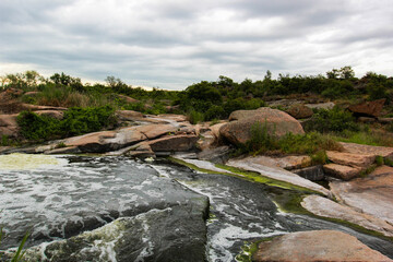 Waterfall flows among high rocks, red stones and cliffs, green bushes and trees