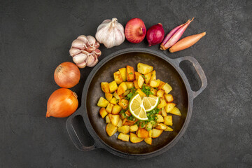 top view tasty fried potatoes inside pan with lemon and garlics around on the dark background color calorie cuisine meal food