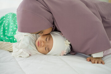 Muslim new born baby girl wearing HIJAB with sister kissing sleeping on white bed at home. 