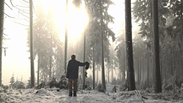 Snowboarder stands in foggy snowed in forest with sun shining through trees and lensflares shot in 4k super slow motion