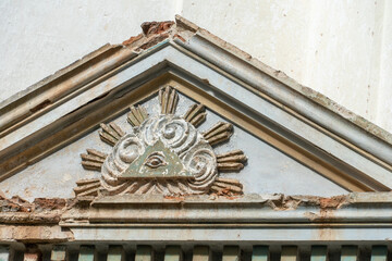 Masonic symbol on the wall of an ancient dilapidated church. The eye of God in the center of the pyramid rises above the mortal worlds in the rays of the rising sun and shrouded in a haze clouds.